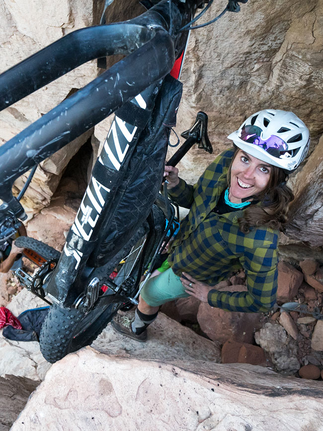 Cairn Project Ambassador Ashley Carruth hands her mountain bike up a steep rock to the photographer