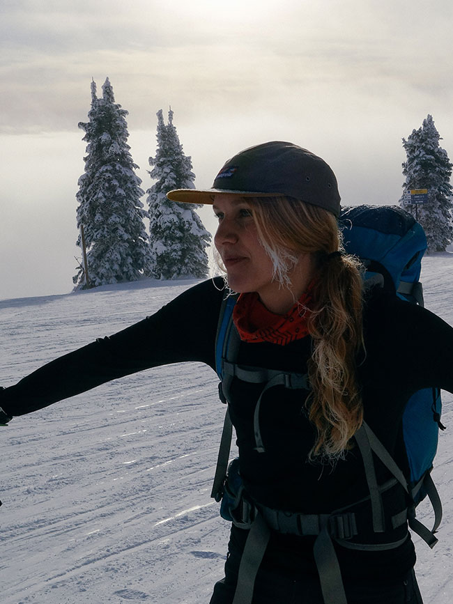 Cairn Project Ambassador Emily Sullivan pauses on a ski tour with snow covered trees behind her