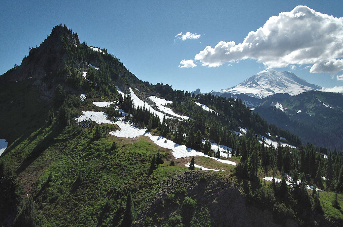 A forested mountain vista view with snow on the north sides of the mountains