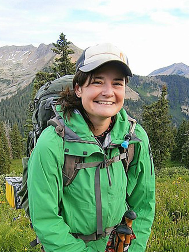 Cairn Project Ambassador Crystal Muzik smiles while wearing a backpack in the mountains