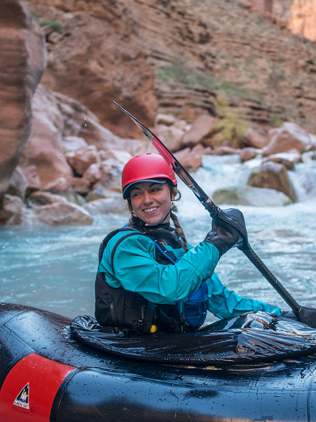 Cairn Project Ambassador Molly Harrison smiles and looks over her shoulder while paddling a solo inflatable raft