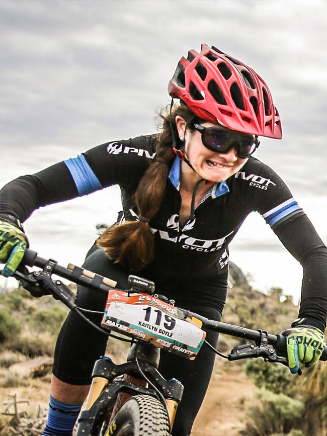 Cairn Project Ambassador Kait Boyle bites her lip in focus while riding a mountain bike in a bike race