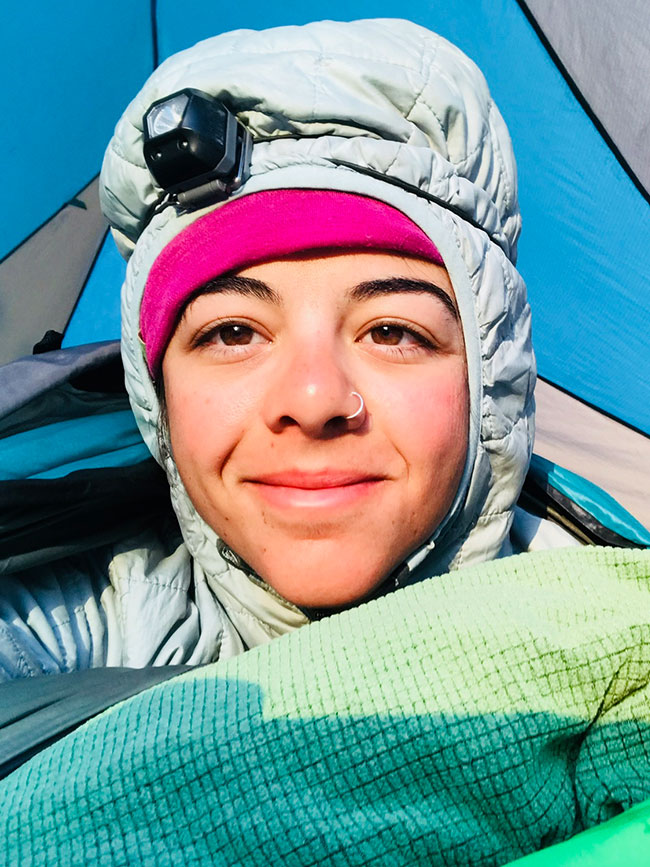 A selfie of Cairn Project Ambassador Rachel Mackey bundled up in a tent with a headlamp over her puffy jacket hood