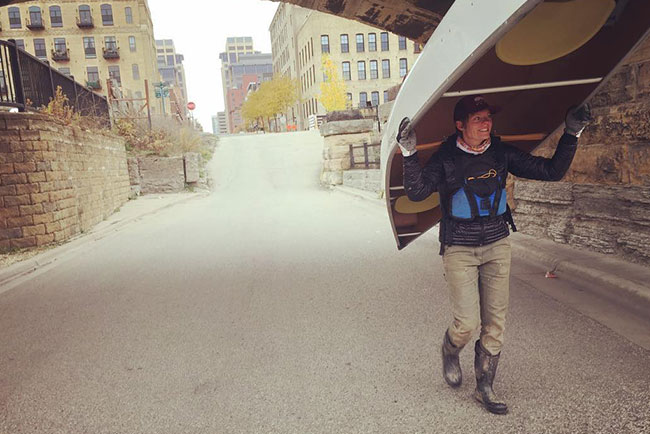 Shannon Conk carries a canoe over her head down a city street