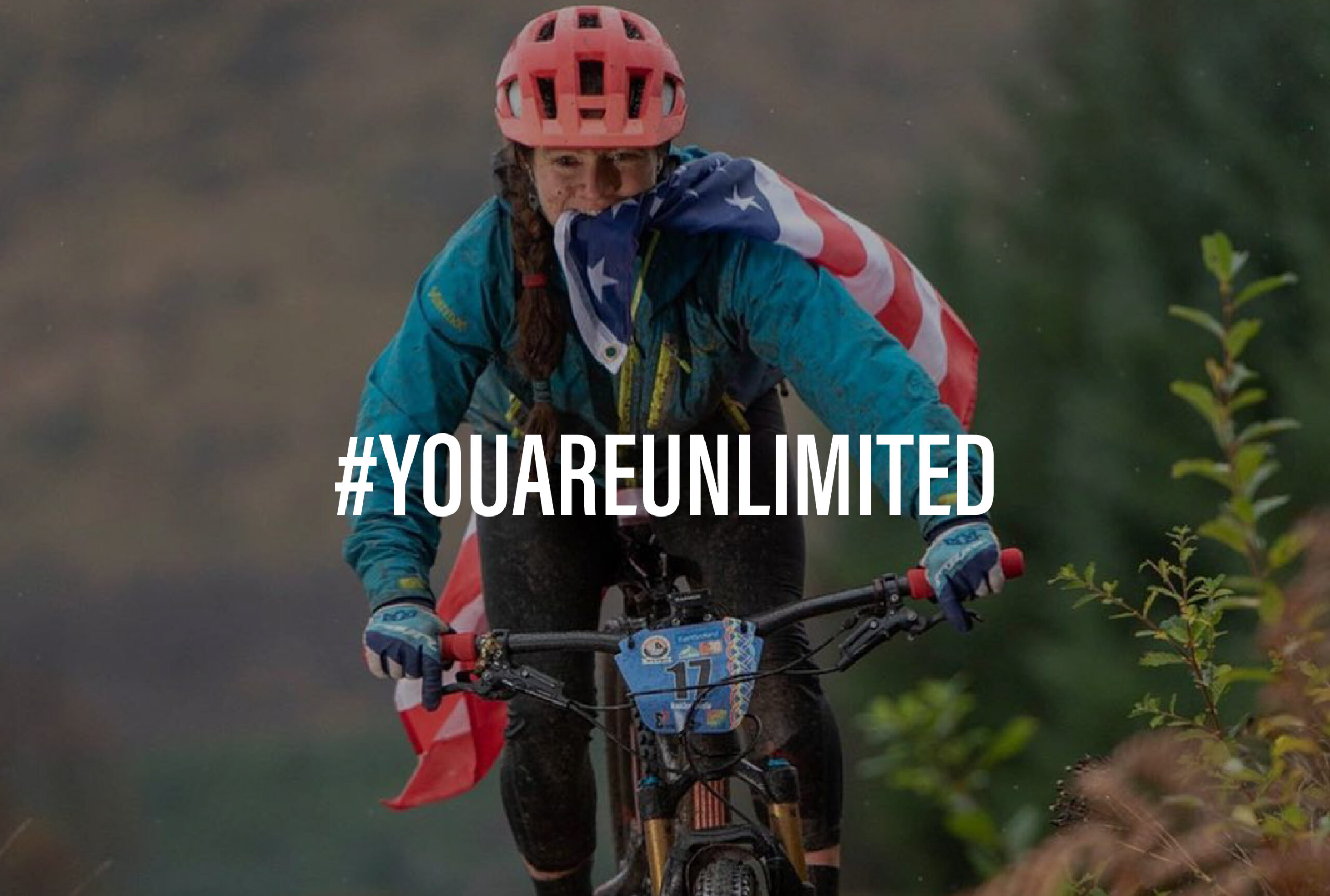 An image of a woman on a bike holding an American flag in her teeth with the words #YouAreUnlimited on top of it