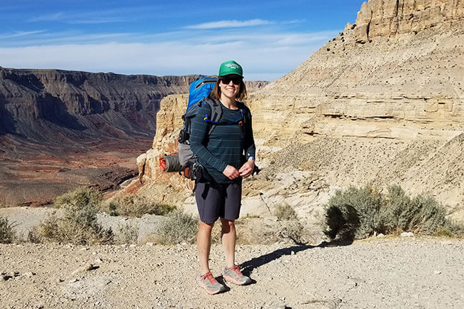 Kristin smiles on the edge of a desert hiking trail wearing a backpack