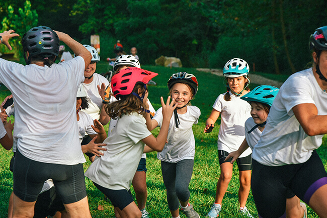 Kids wearing bike helmets play a group game in the grass