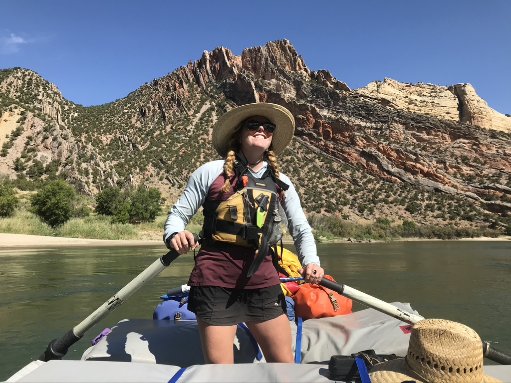 Cairn Project Ambassador Alyssa Winkelman navigates a raft on a river with red rocks behind her