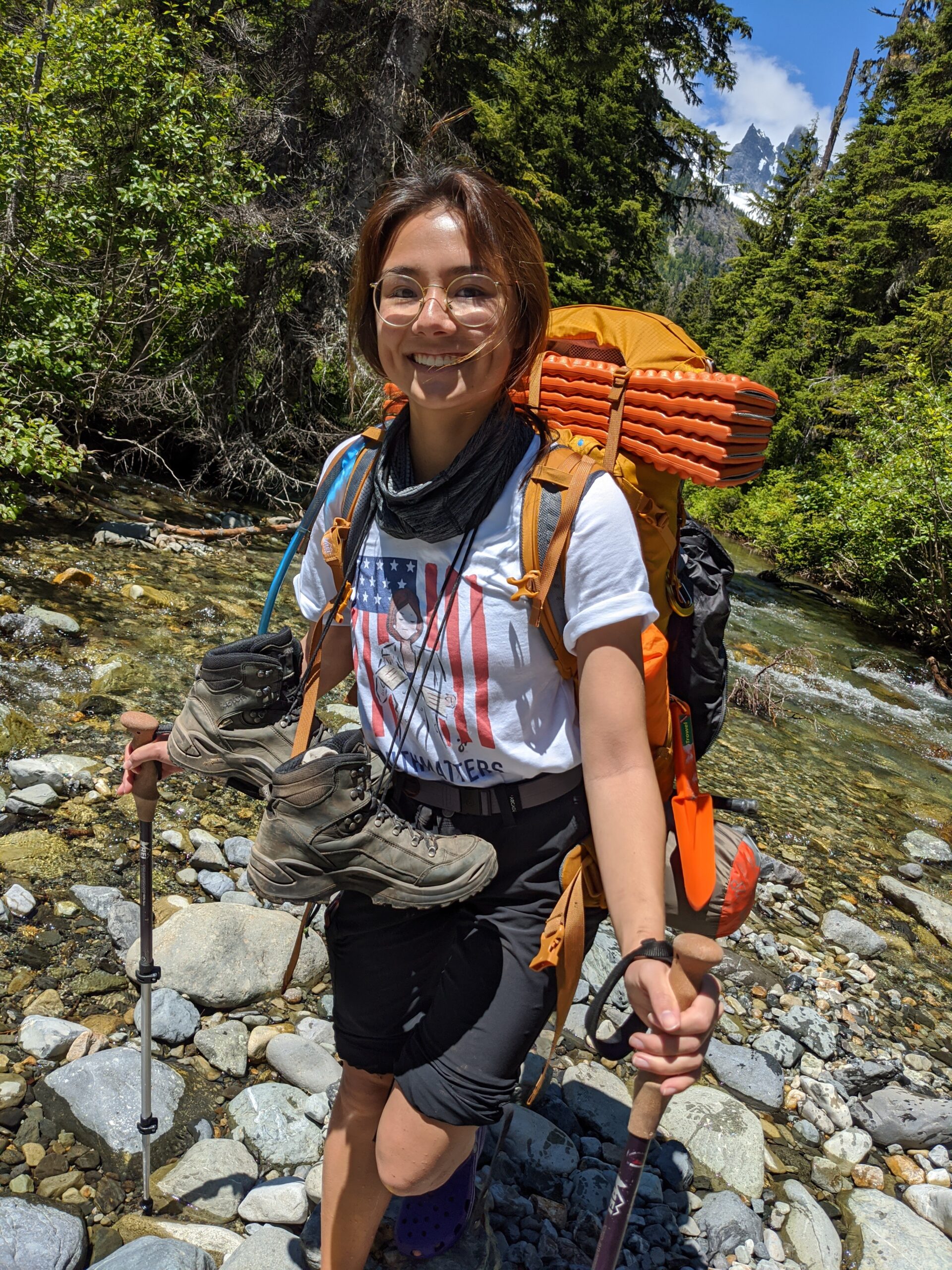 Cairn Project Ambassador Maya Yamaguchi Sullivan smiles wearing a backpack and her hiking boots tied around her neck