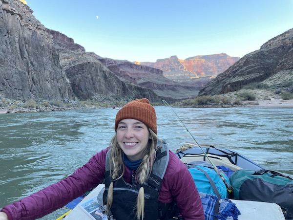 A Cairn Project ambassador smiles from a raft on a river with orange desert peaks behind her
