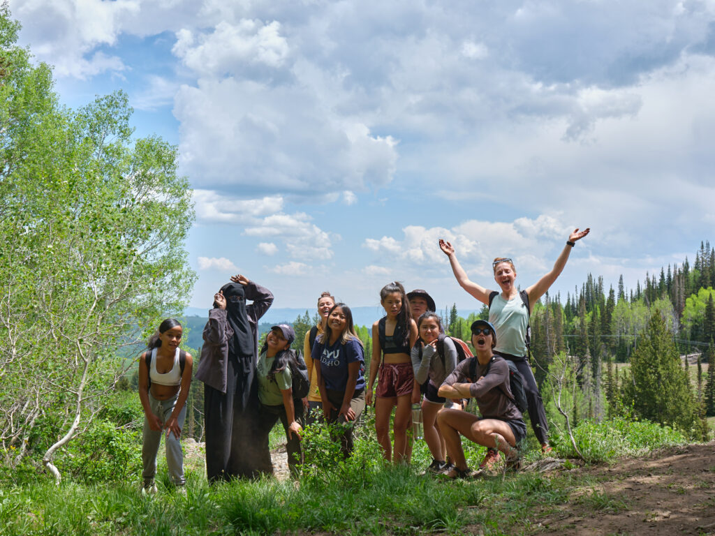 A group of girls poses for a group photo on the side of a hiking trail surrounded by aspens