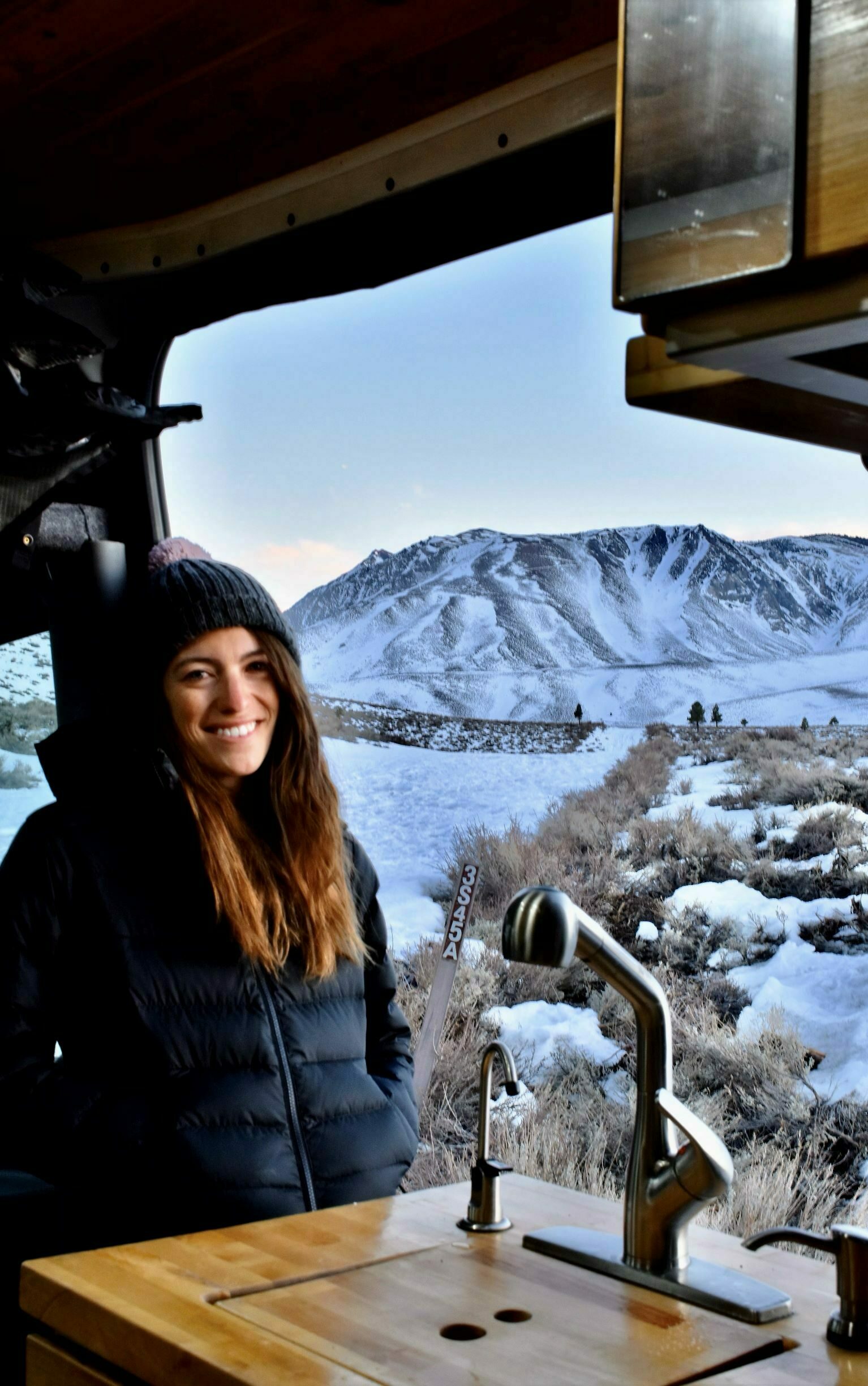 Cairn Project Ambassador Lauren Mathews sits in a converted van with snowy mountains behind her