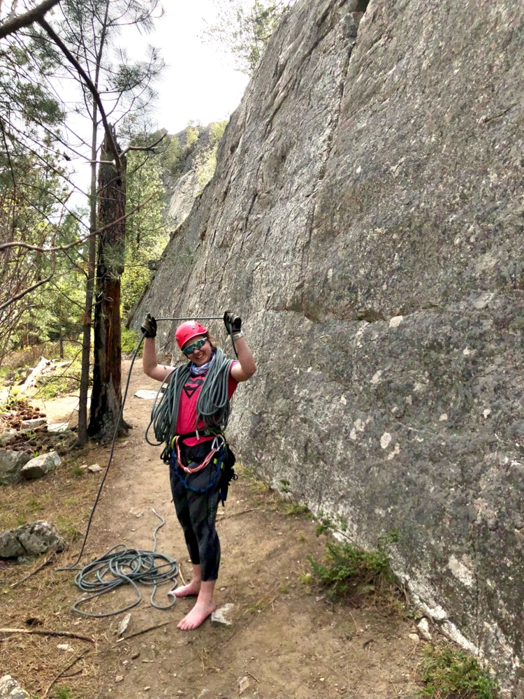 Dana ringler flecks rope over her head, there is a rock wall behind her