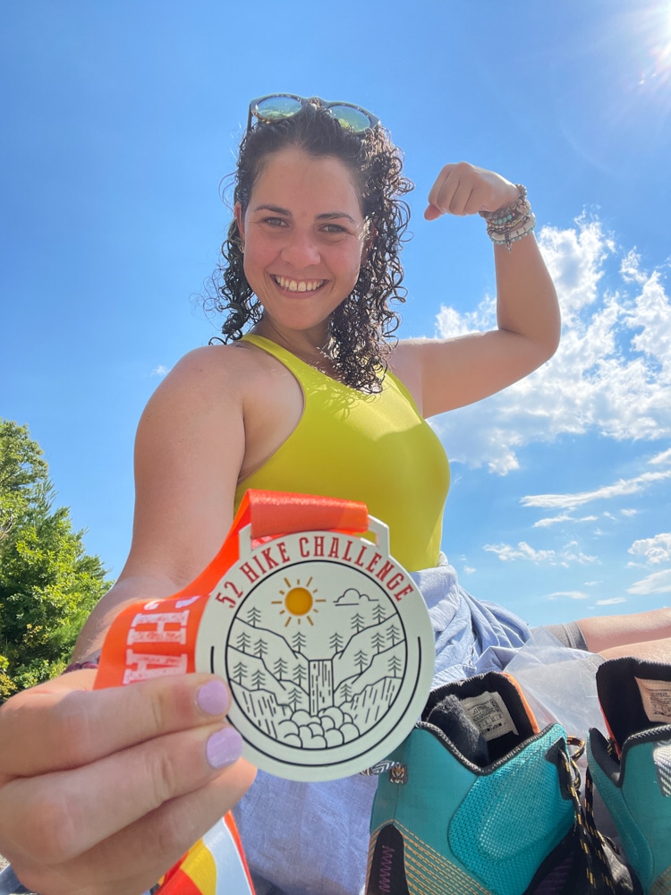 Cairn Project Ambassador Suleyka Garcia Rivera, a latina women, looks at the camera and smiles while holding a medal and raising her back arm up to show off her muscles. 
