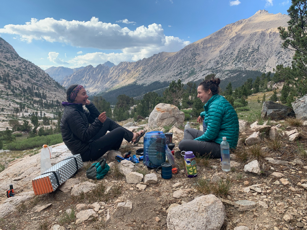 two friends sit in the mountains enjoying a snack